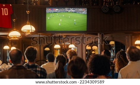 Group of Soccer Fans Watching a Live Football Match Broadcast in a Sports Pub on TV. People Cheering, Supporting Their Team. Crowd Goes Ecstatic When Team Scores a Goal and Wins the Championship. Royalty-Free Stock Photo #2234309589