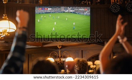 Group of Soccer Fans Watching a Live Football Match Broadcast in a Sports Pub on TV. People Cheering, Supporting Their Team. Crowd Goes Ecstatic When Team Scores a Goal and Wins the Championship. Royalty-Free Stock Photo #2234309615