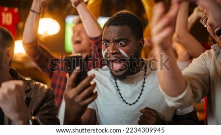 Portrait of an Excited Young Black Man Holding a Smartphone, Anxious About a Sports Bet on His Favorite Soccer Team. Lively Successful Emotions When Football Team Scores a Winning Goal. Royalty-Free Stock Photo #2234309945