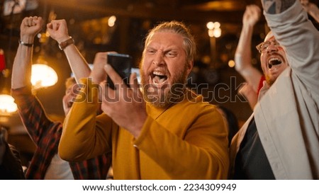 Excited Masculine Man Holding a Smartphone, Feeling Nervous About the Sports Bet He Put on a Favorite Soccer Team. Ecstatic When Football Team Scores a Goal and He Wins a High Stakes Casino Prize. Royalty-Free Stock Photo #2234309949