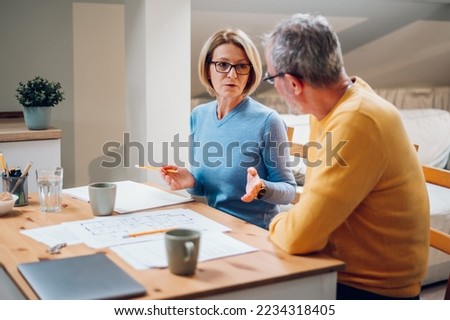 Senior couple enjoying their time at home and examining housing plans while relocating into a new house. Elderly couple moving into a new house. Investing in the new property. Focus on a woman. Royalty-Free Stock Photo #2234318405
