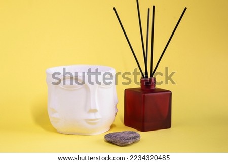 Buddha white vase on yellow background with Burgundy glass jar for aroma therapy and stone