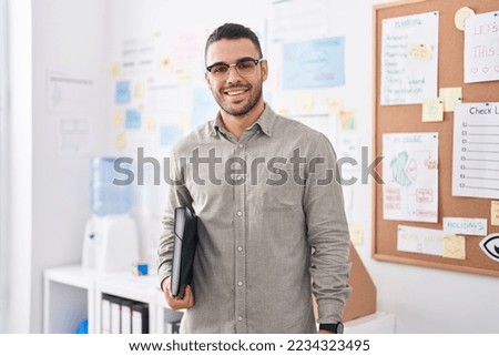 Young hispanic man business worker smiling confident holding binder at office Royalty-Free Stock Photo #2234323495