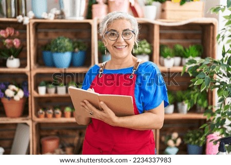Middle age grey-haired woman florist smiling confident writing on notebook at florist
