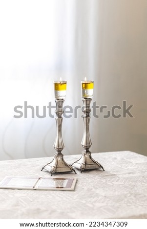 A pair of Shabbat candles are lit with oil on silver candlesticks on the Shabbat table. Royalty-Free Stock Photo #2234347309