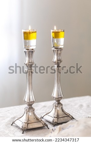 A pair of Shabbat candles are lit with oil on silver candlesticks on the Shabbat table. Royalty-Free Stock Photo #2234347317