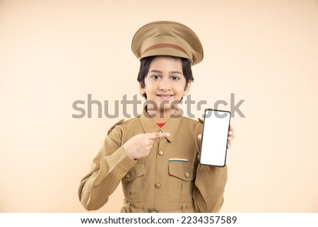 Young elementary indian boy kid wearing police uniform showing smart phone with blank white screen to put advertisement or promotion isolated on beige studio background.