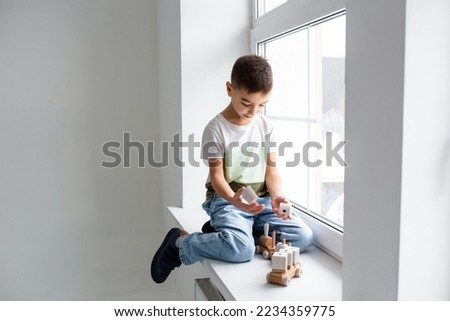 A preschooler boy plays with a wooden toy train on the windowsill