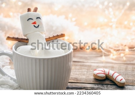 Close up, mug of hot drink with marshmallow snowman on blurred background.
