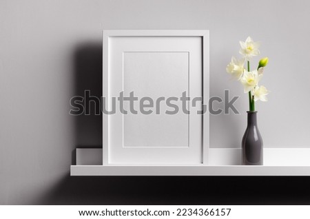 Empty portrait picture frame mockup on white shelf with flowers