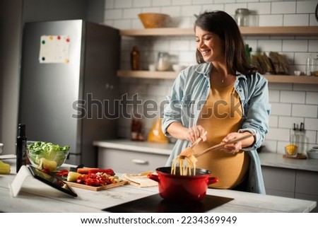 Beautiful pregnant woman preparing delicious food. Smiling woman cooking pasta at home Royalty-Free Stock Photo #2234369949