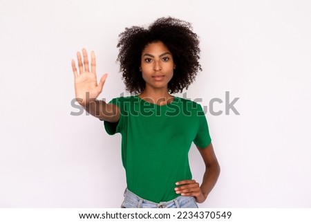 Portrait of confident young woman making denial gesture over white background. African American lady wearing green T-shirt and jeans showing stop symbol. Forbiddance concept
