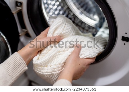 Woman putting white clothes into the drum of a washing machine, front view. Washing dirty clothes in the washer Royalty-Free Stock Photo #2234373561