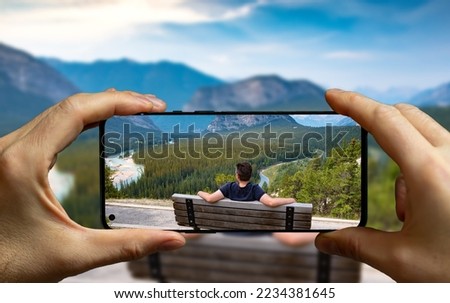 Tourist taking a picture with a mobile phone of a man resting on a bench at the Banff national park.
