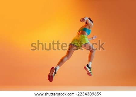 Back view. Sportive muscled woman, professional runner running away isolated on yellow background in neon light. Sport, fitness, competition, speed and active lifestyle. Copy space for ad. Sunset Royalty-Free Stock Photo #2234389659