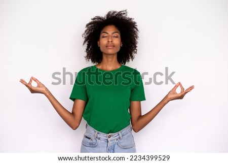 Portrait of relaxed young woman doing yoga over white background. African American lady wearing green T-shirt and jeans meditating with closed eyes. Harmony and exercise concept Royalty-Free Stock Photo #2234399529