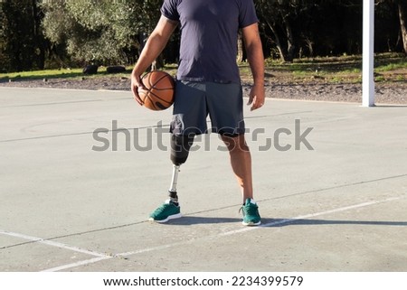 Strong man with artificial leg standing at sports ground in city park on sunny day. Basketball player with physical disability doing sports outside. Amputee sport, active lifestyle concept