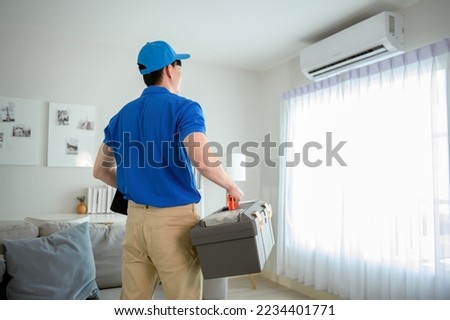 An Asian young Technician service man wearing blue uniform checking ,  cleaning air conditioner in home Royalty-Free Stock Photo #2234401771
