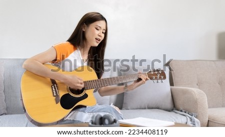 Woman practicing or learning to play guitar and practice using his fingers to hold guitar chords while looking at music notes with intention, Taking advantage of free time, Relax during free time. Royalty-Free Stock Photo #2234408119