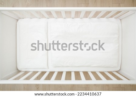 Empty white baby crib with mattress, sheet, pillow and blanket. Closeup. Top view. Royalty-Free Stock Photo #2234410637