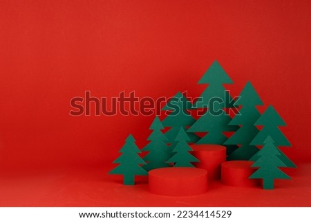 Festive Christmas background with three red cylinder podiums mockup, green paper spruces in art style for presentation cosmetic product, gifts, goods, copy space. New Year template for advertising.