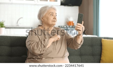 Senior woman getting angry, making video call with relatives, looking at camera and waving, sitting on comfortable sofa. Old woman who gets very angry with the person she is talking to on the phone. 