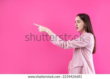 Happy young caucasian female in a pink jacket pointing fingers away