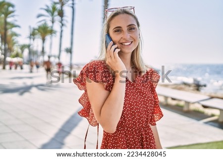 Young blonde girl smiling happy talking on the smartphone at the promenade.