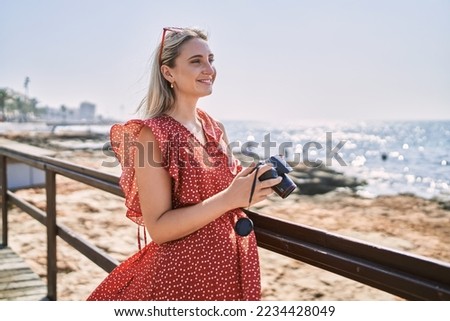 Young blonde girl smiling happy using camera at the beach