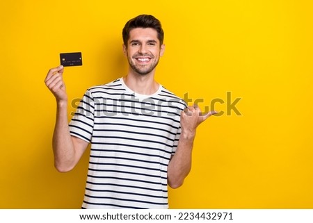 Photo of cheerful nice man toothy smile hold debit card direct finger empty space isolated on yellow color background