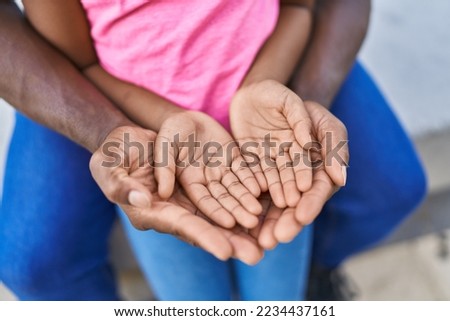 Father and daughter sitting on bench with hands together at street