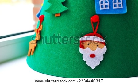 On the windowsill is a felt Christmas tree with toys. Focus on santa claus toy. Horizontal photo