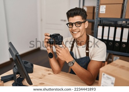 Young hispanic man ecommerce business worker using professional camera at office