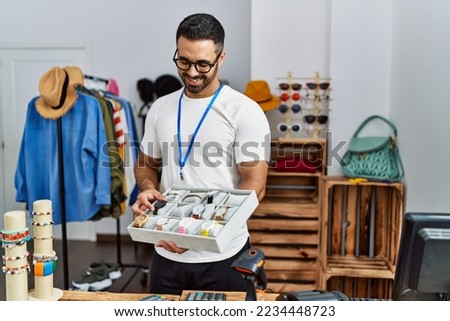 Young hispanic man shopkeeper showing watch working at clothing store
