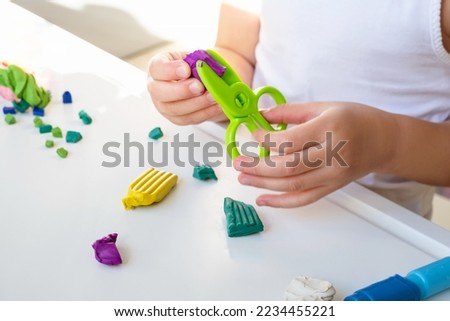 Girl toddler holds green toy scissors by one hand and plasticine by other hand. Mold in shape playing clay. Kid fines motor skills and crafting education using toy plasticine. Royalty-Free Stock Photo #2234455221