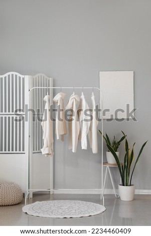 Rack with stylish warm sweaters and houseplants in room