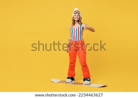 Snowboarder satisfied woman wear orange suit goggles mask hat ski costume swimsuit spend extreme weekend show thumb up isolated on plain yellow background studio. Winter sport hobby trip relax concept