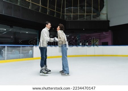 Side view of cheerful interracial couple spending time during date on ice rink 