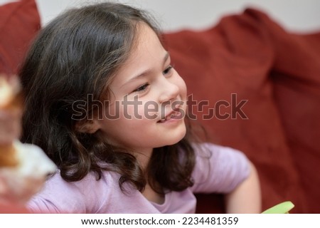 expressive young girl is eating chicken and vegetables for dinner on the couch while watching TV