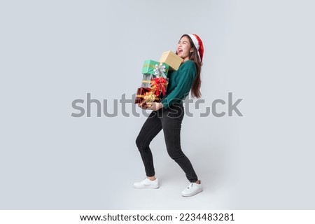 Full length Asian woman in casual green sweater and christmas santa hat lifting a gifts box on isolated grey background. Happy anniversary or new year festival concept.