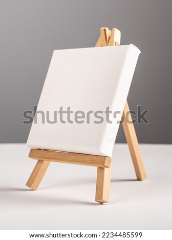 Empty blank white canvas mockup standing on mini wood tripod easel on desk. High quality photo