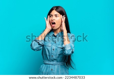 young hispanic casual woman feeling happy, excited and surprised, looking to the side with both hands on face