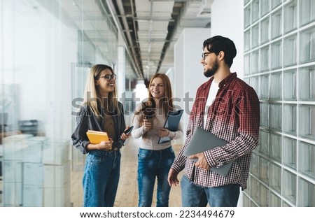Group of friendly diverse employees wearing casual outfits discussing work issues while standing in spacious glassy office hallway during workday Royalty-Free Stock Photo #2234494679
