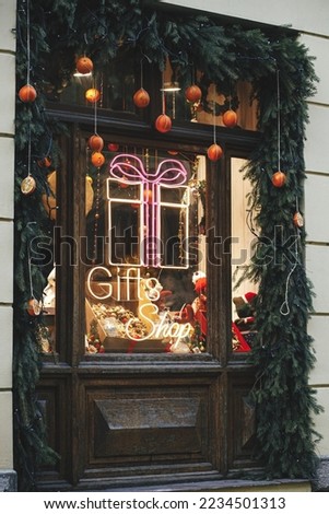 Stylish Christmas fir branches with baubles and neon sign gift shop on building exterior. Modern christmas decor in city street. Winter holidays in Europe. Merry Christmas