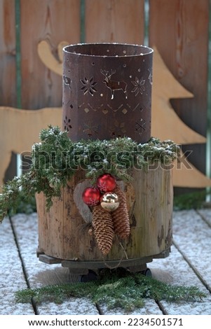 christmas decoration on a tree trunk with juniper twigs, spruce cone, christmas bells and a iron decor at a snowy winter day                                    