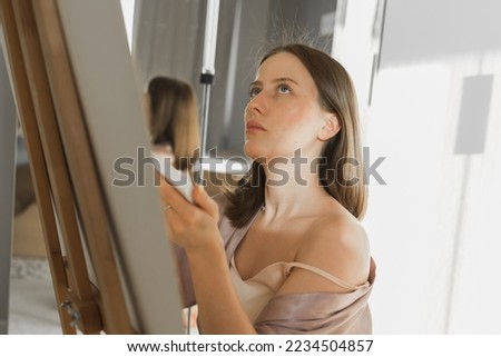 Young woman artist painting on canvas on the easel at home in bedroom - art and creativity concept