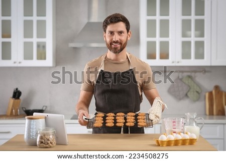 Man holding grid with freshly baked cookies in kitchen. Online cooking course Royalty-Free Stock Photo #2234508275