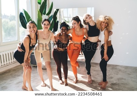 Group of multiracial positive sportswomen in easy activewear standing together near window in spacious fitness studio and enjoying photo session Royalty-Free Stock Photo #2234508461