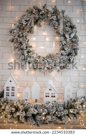A traditional bright Christmas wreath hanging over the fireplace, on a white brick wall, and decor small houses on a fireplace. Christmas concept, new year. . High quality photo