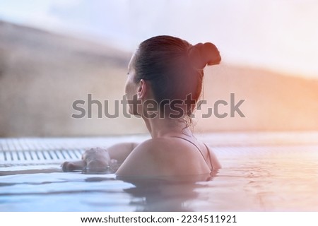 Woman enjoying view, relaxing in outdoor thermal pool on a winter day. Snowy mountains on the background. Royalty-Free Stock Photo #2234511921